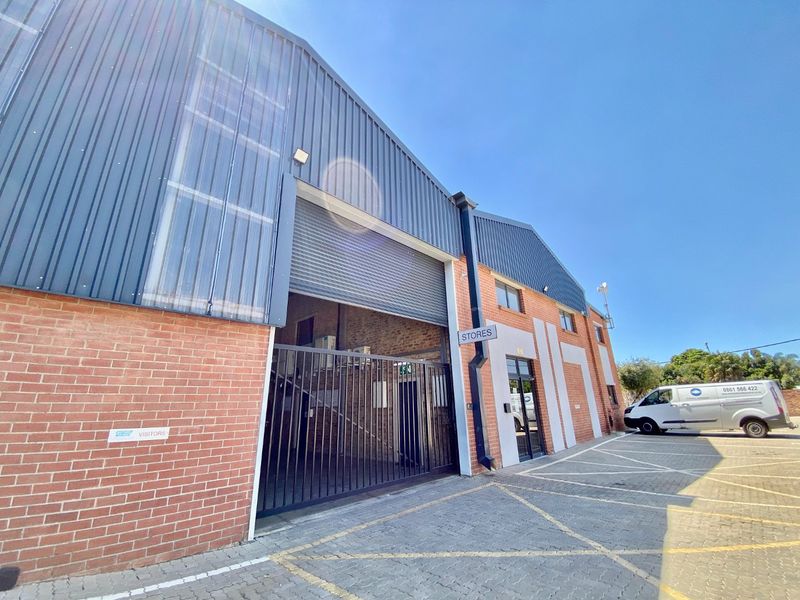 Industrial warehouse exterior featuring a brick and metal facade, roller shutter door access, and a paved parking area.