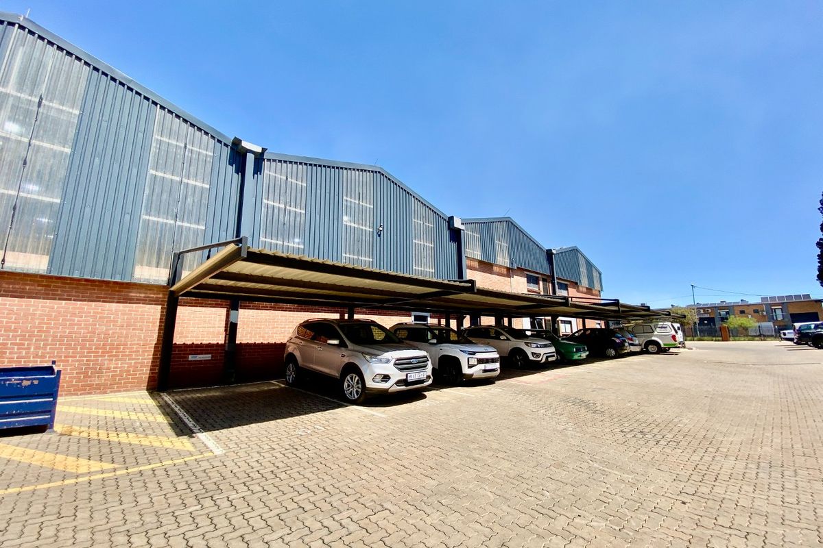 Industrial property exterior featuring a brick and corrugated metal facade with an extensive covered parking area and paved driveway.
