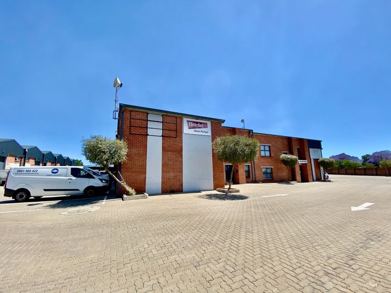 Front elevation of an industrial property featuring a face brick facade, paved parking area, and prominent commercial signage.