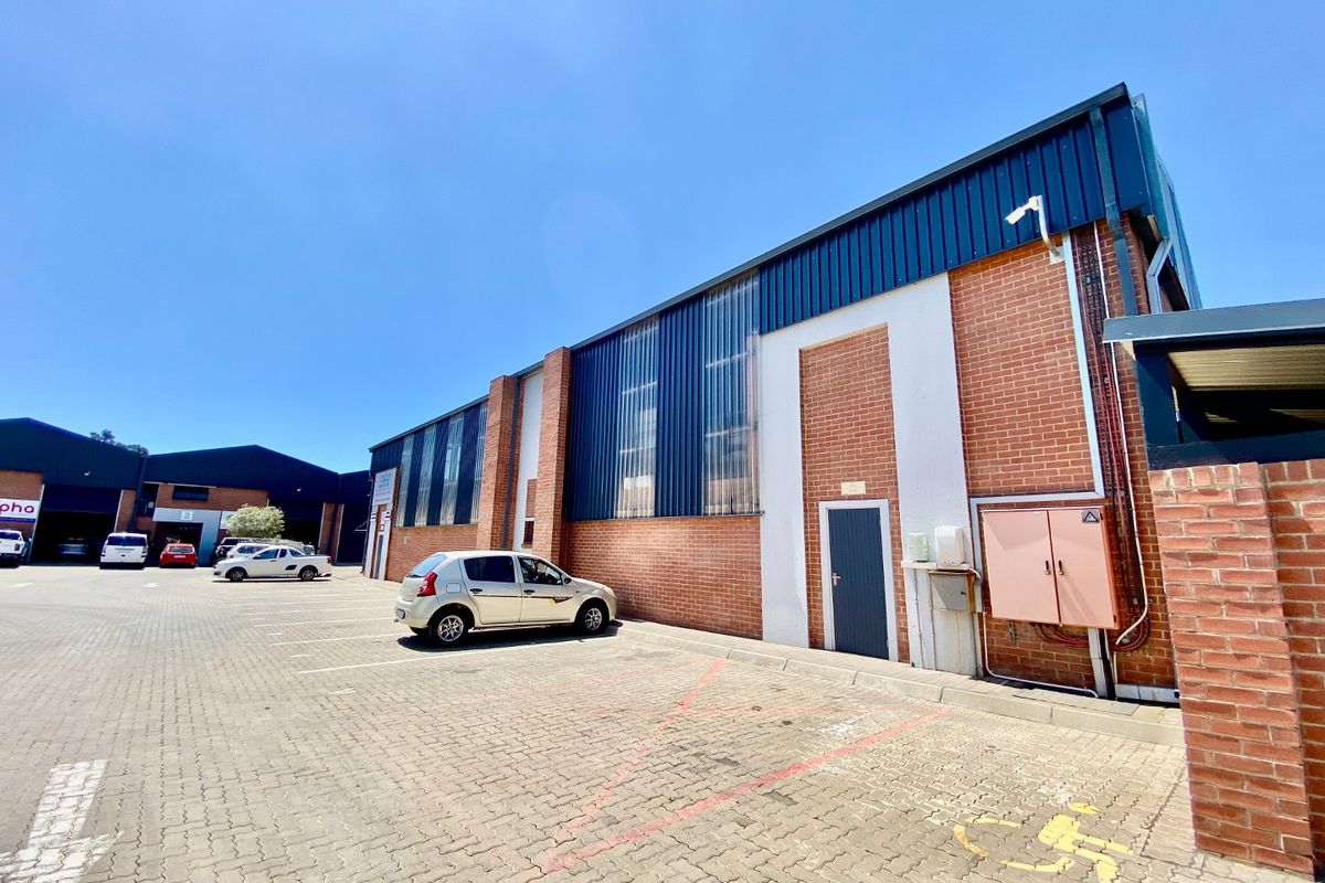 Exterior view of an industrial property featuring a brick and metal facade with a paved parking area and integrated security infrastructure.