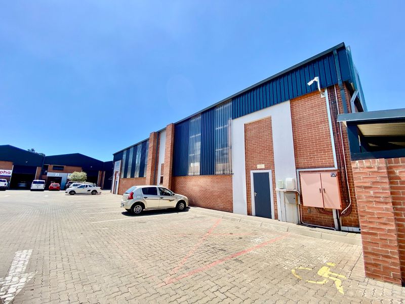 Exterior view of an industrial property featuring a brick and metal facade with a paved parking area and integrated security infrastructure.