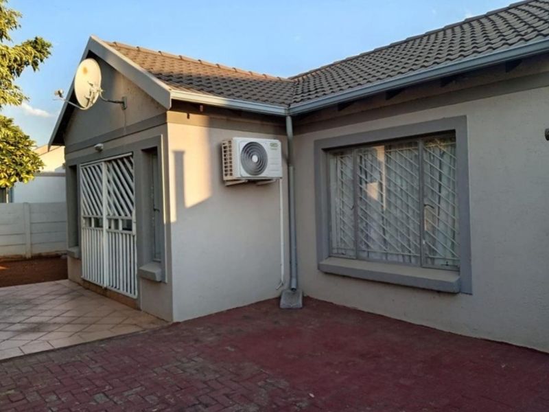 Rear exterior view of the townhouse featuring a paved patio area, security gates, and an installed air conditioning unit.