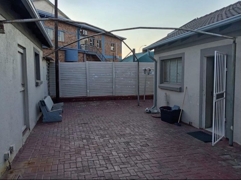 A paved rear courtyard area featuring a metal frame structure, security gate, and perimeter walling, providing a functional outdoor space.