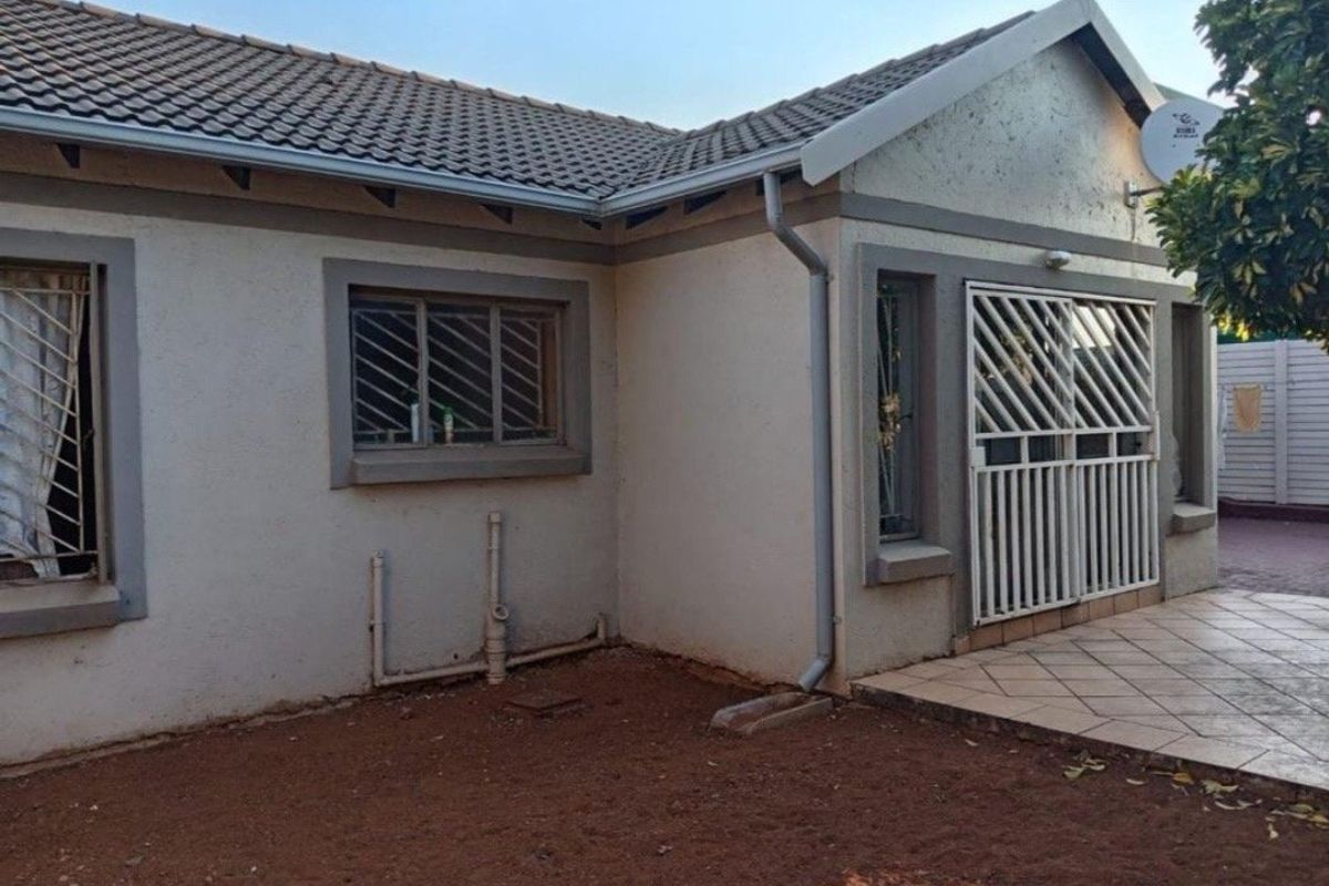 Rear exterior view of the townhouse featuring a tiled patio, security gates, and exposed plumbing along the exterior wall.