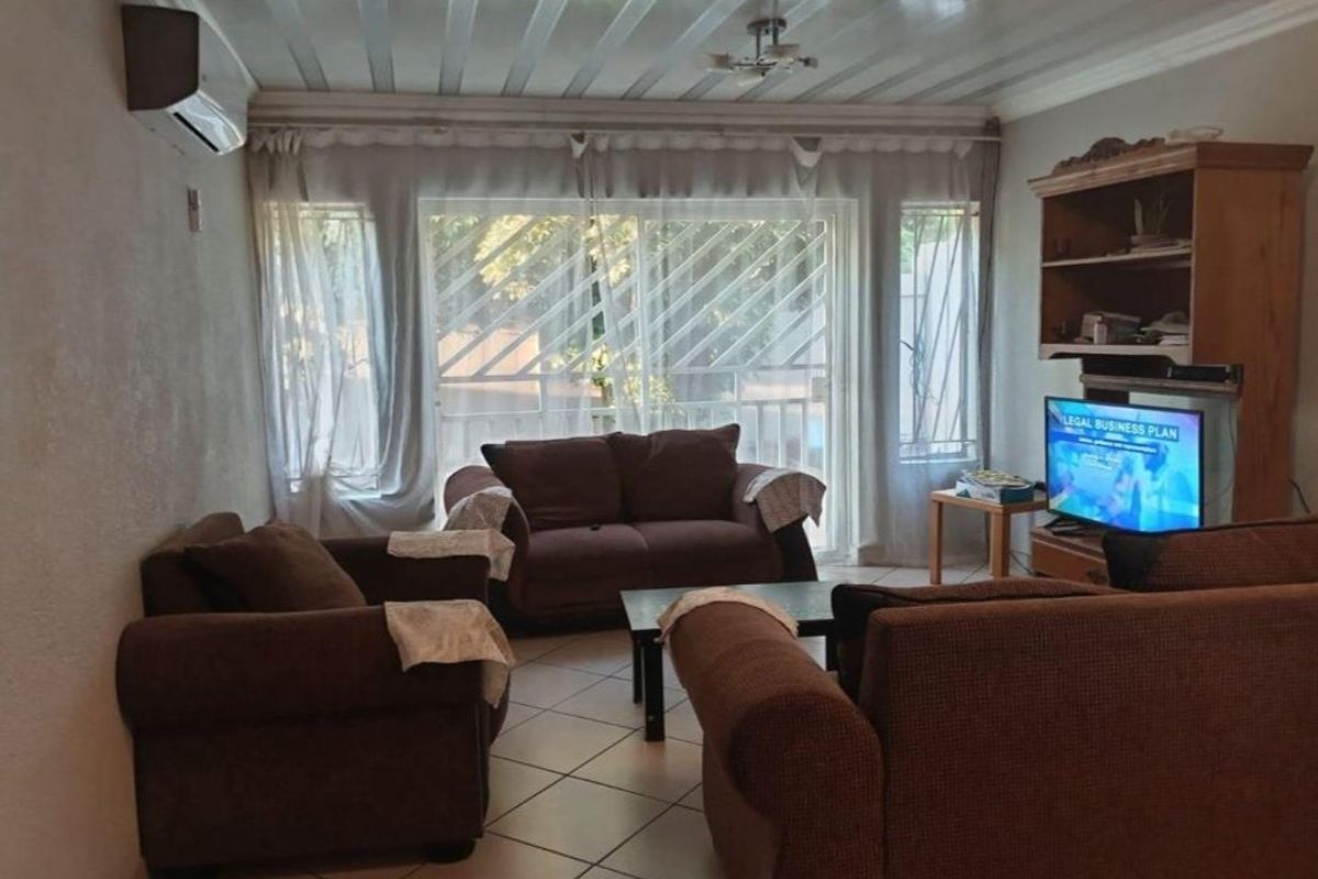 A living room featuring tiled flooring, a wall-mounted air conditioning unit, and a sliding glass door with security bars leading to the exterior.