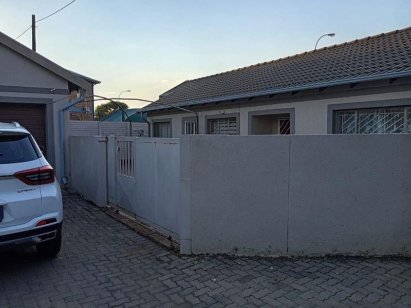 Front exterior view of a townhouse featuring a paved driveway, perimeter wall with security gate, and a tiled roof structure.