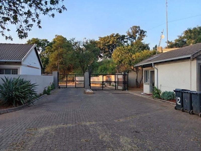 Front entrance view of the townhouse complex featuring a paved driveway, security gate, and perimeter walling.