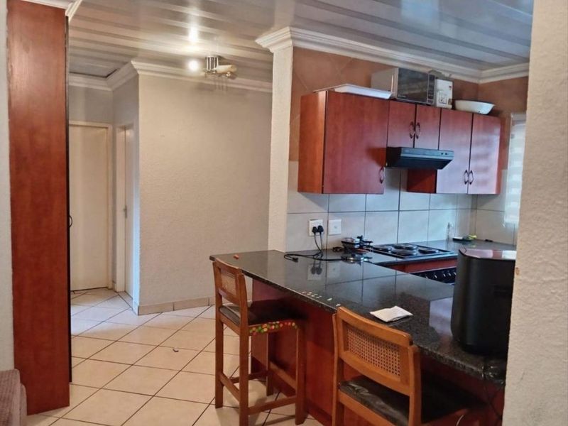 A functional kitchen featuring wooden cabinetry, granite countertops, a built-in hob with extractor fan, and tiled flooring, opening into a hallway area.