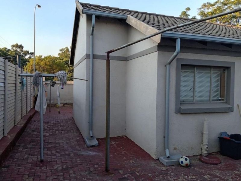 Rear exterior view of the townhouse featuring a paved courtyard, tiled roof, and functional drainage system with downpipes.