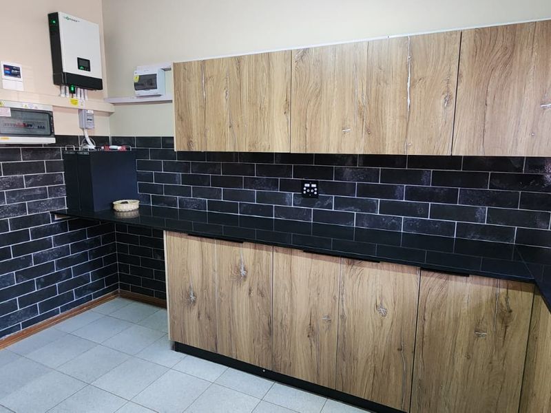 A functional scullery featuring modern wood-grain cabinetry, black subway tile backsplash, dark stone countertops, and integrated solar power infrastructure.