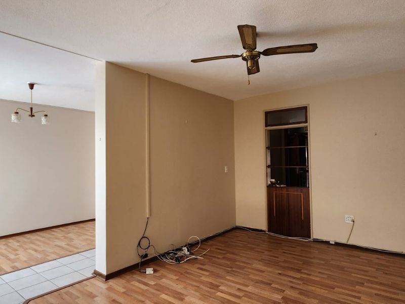 An empty living area featuring laminate and tiled flooring, a ceiling fan, and neutral wall finishes, offering a blank canvas for renovation.