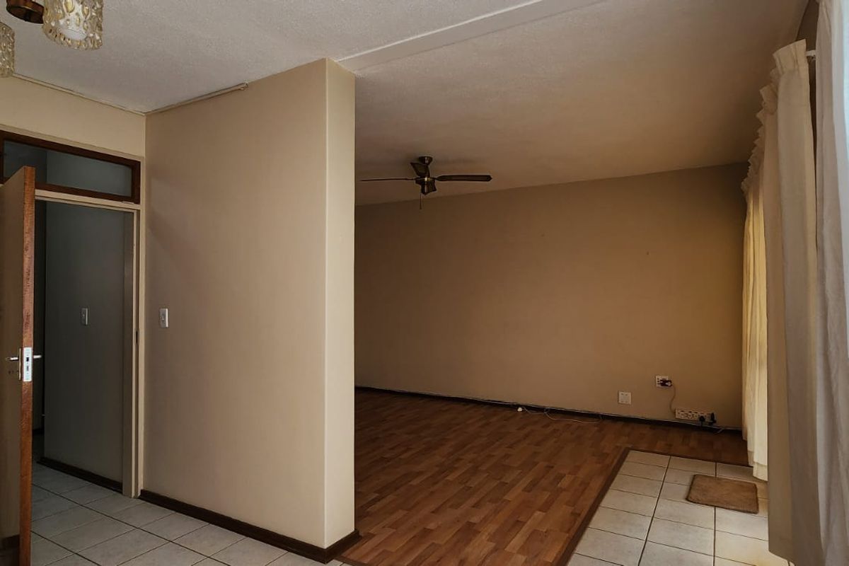 An empty living area featuring a mix of tiled and laminate flooring, a ceiling fan, and neutral wall tones.