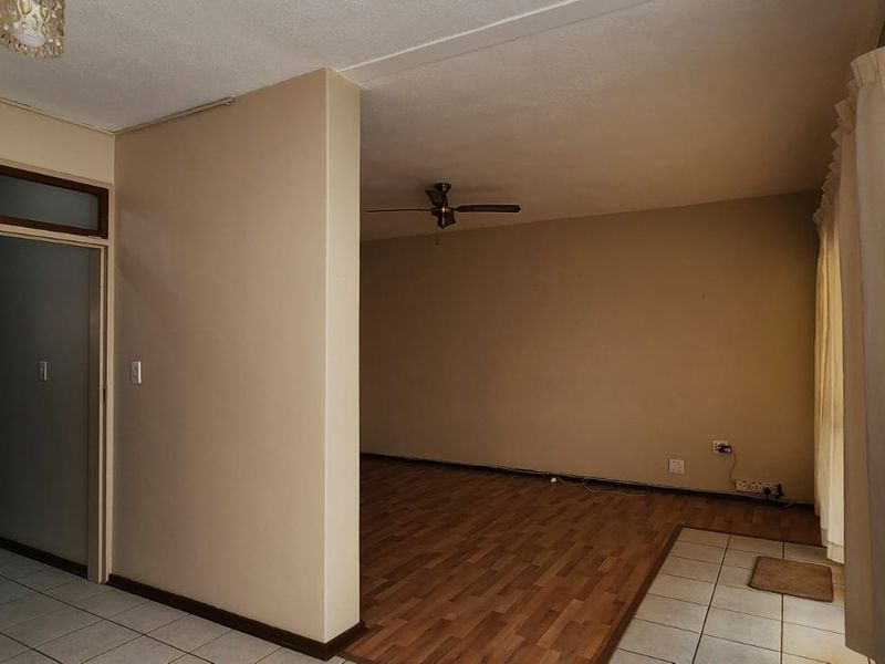 An empty living area featuring a mix of tiled and laminate flooring, a ceiling fan, and neutral wall tones.