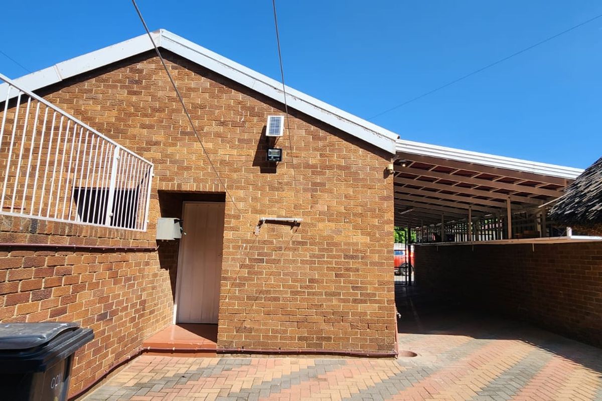 Rear exterior view featuring a face brick facade, paved driveway, and a covered carport area.