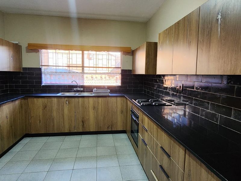 A functional kitchen featuring wood-look cabinetry, black subway tile backsplash, granite countertops, and built-in cooking appliances.