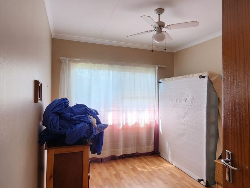 A simple bedroom featuring laminate flooring, a ceiling fan, and a large window, offering a blank canvas for personalization.