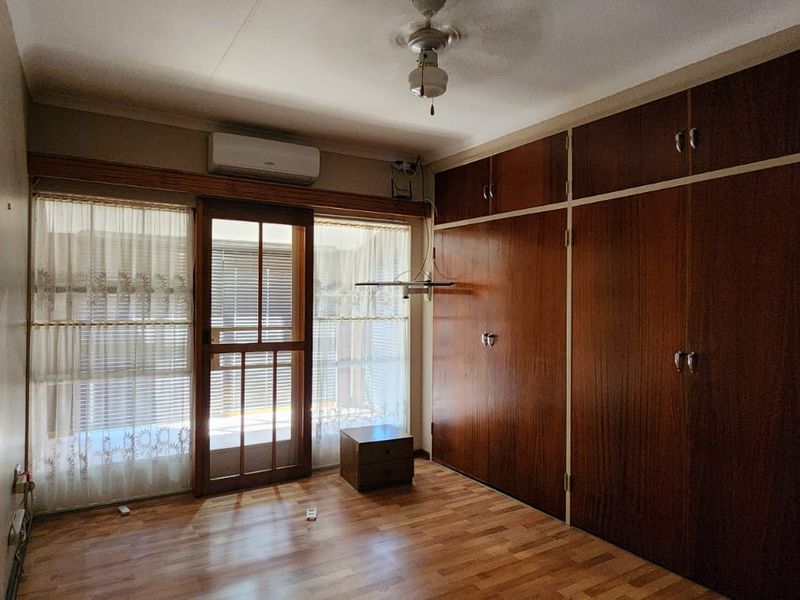 A bedroom featuring built-in wooden cupboards, laminate flooring, a ceiling fan, and a split-system air conditioner with access to an outdoor area.