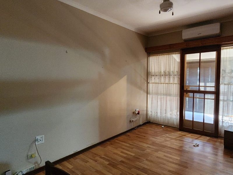 A vacant bedroom featuring laminate flooring, a split-system air conditioner, and a timber-framed glass door leading to an outdoor area.