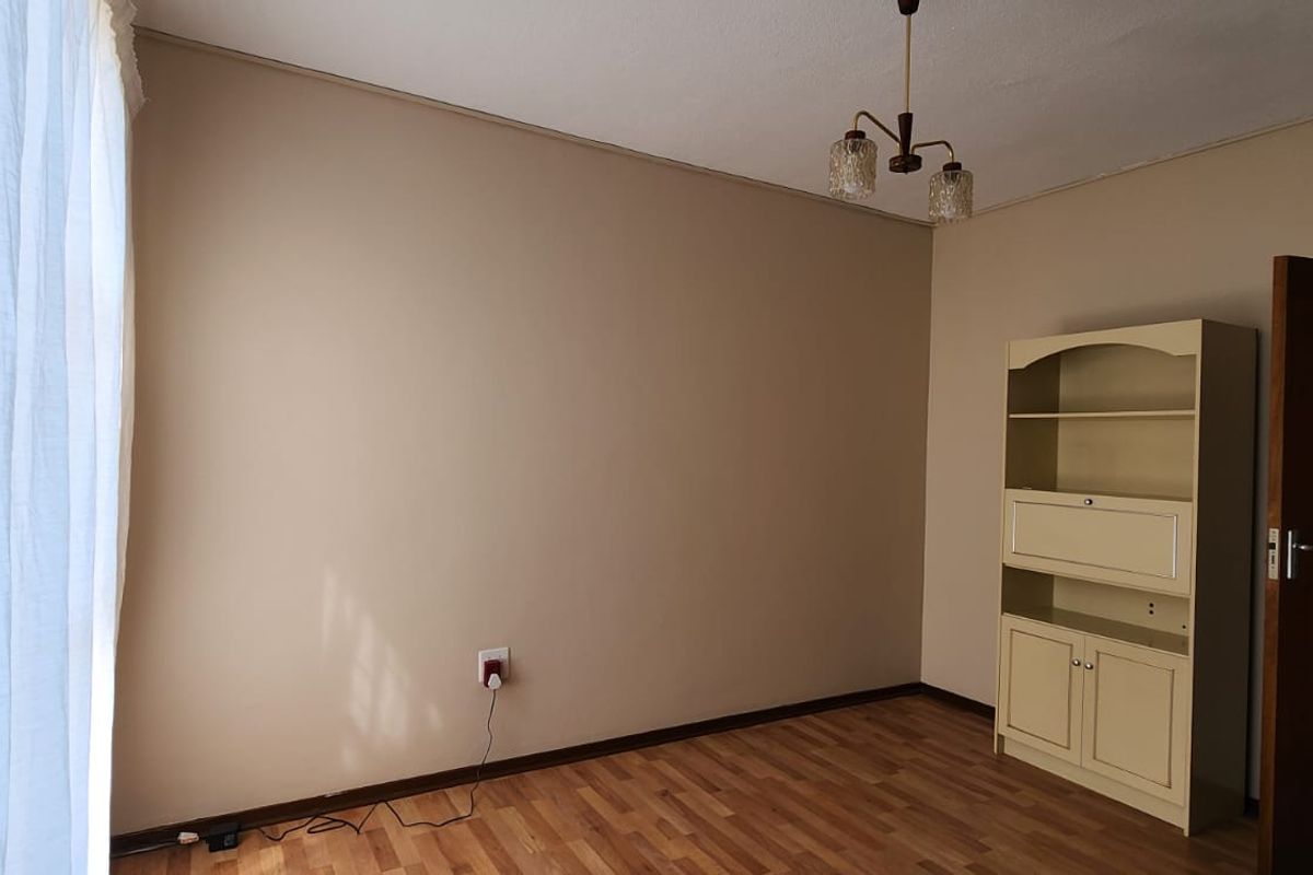 A clean, empty bedroom featuring laminate flooring, neutral wall tones, and a central ceiling light fixture, offering a versatile space for personalization.