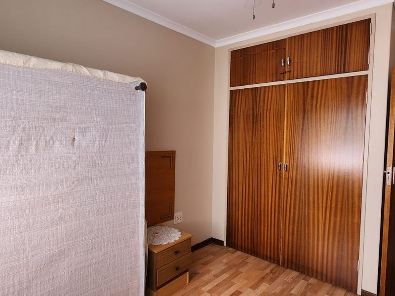 A bedroom featuring built-in wooden cupboards and laminate flooring, offering a functional space with classic finishes.