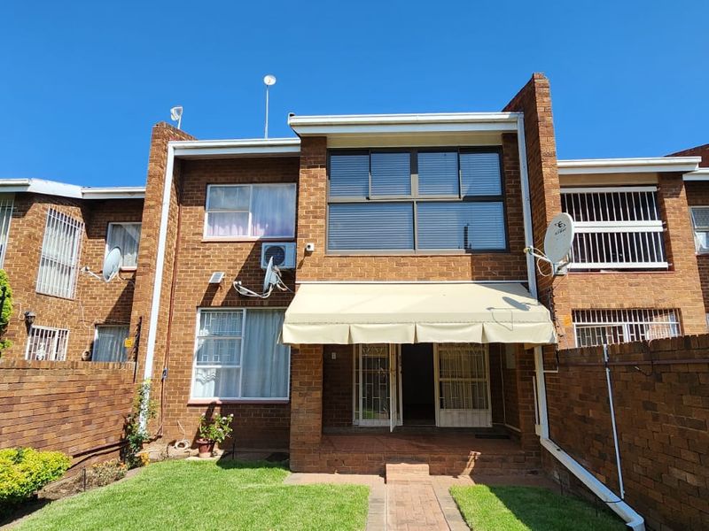 Rear view of a face brick townhouse featuring a private garden, paved walkway, and a retractable awning over the patio entrance.