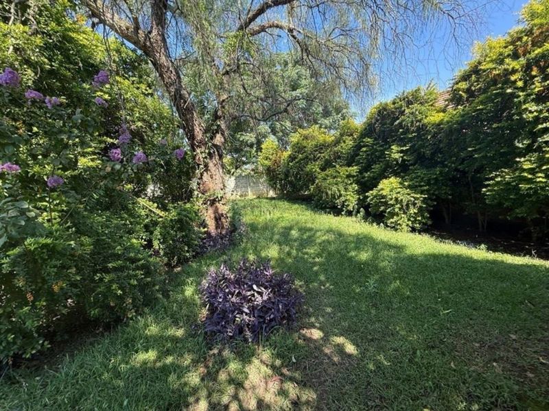 A lush, established garden featuring mature trees, a well-maintained lawn, and dense perimeter greenery providing a private outdoor setting.