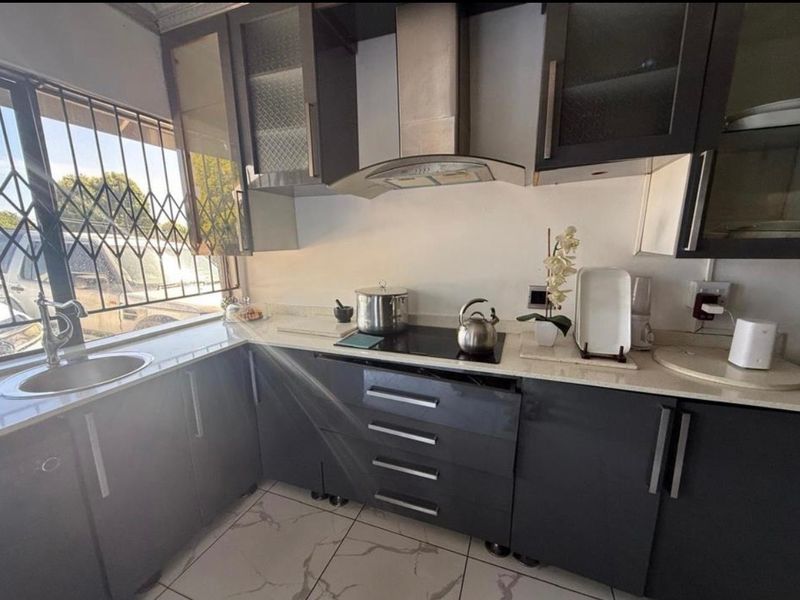 A modern kitchen featuring dark cabinetry, stone countertops, an integrated electric hob with extractor fan, and tiled flooring.