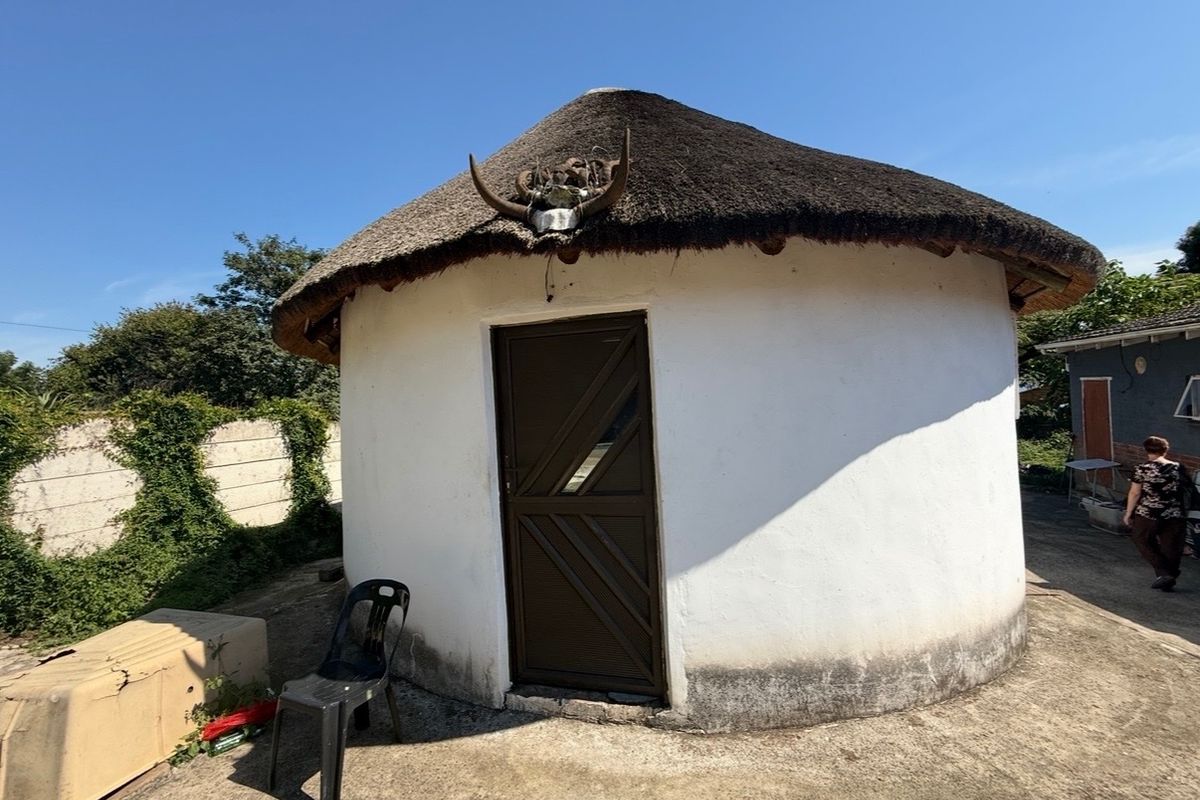 A traditional circular thatched-roof structure with a concrete apron and surrounding precast boundary wall.