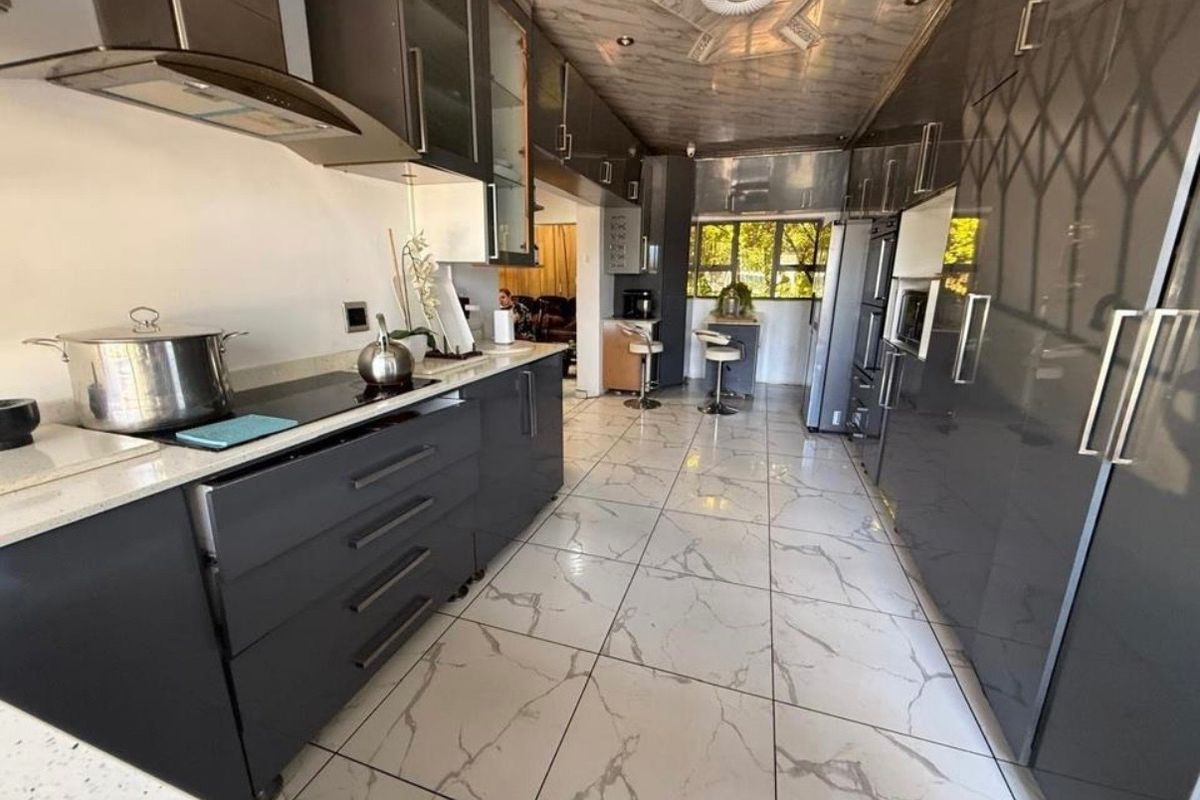 Modern galley-style kitchen featuring high-gloss dark cabinetry, stone countertops, integrated appliances, and polished marble-look floor tiles.