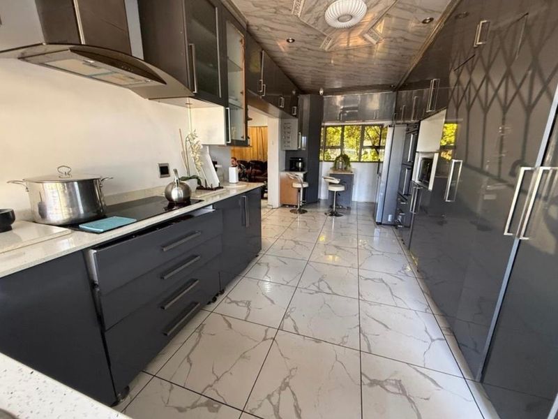 Modern galley-style kitchen featuring high-gloss dark cabinetry, stone countertops, integrated appliances, and polished marble-look floor tiles.