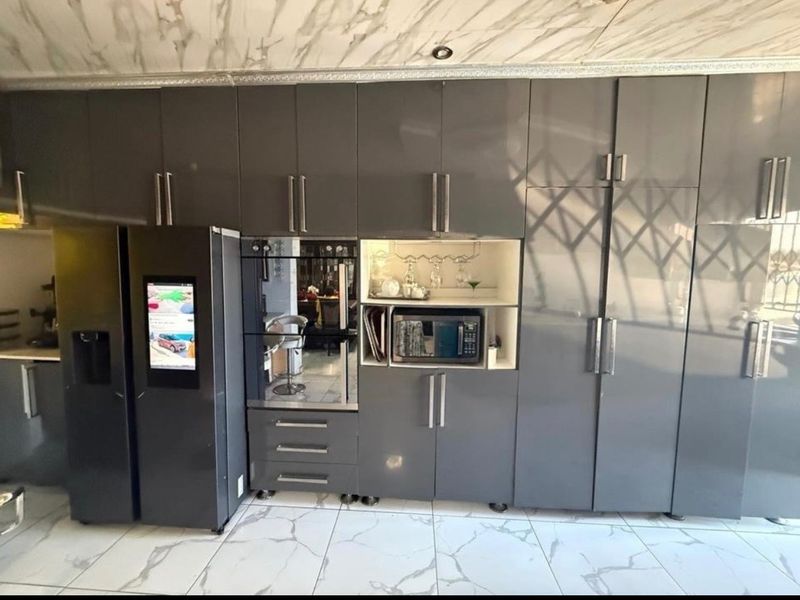 Modern kitchen featuring high-gloss grey cabinetry, integrated appliances, and marble-look floor and ceiling finishes.