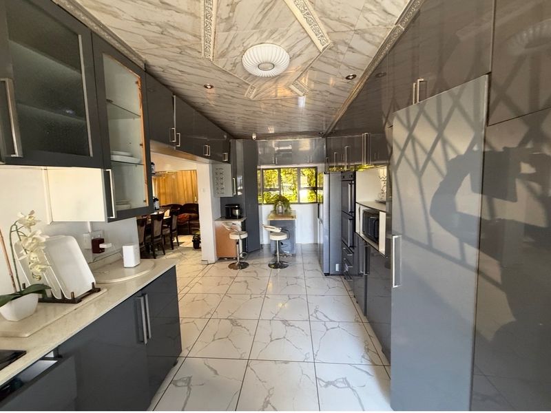 Modern kitchen featuring high-gloss grey cabinetry, stone countertops, and distinctive marble-effect floor and ceiling finishes with integrated appliances.