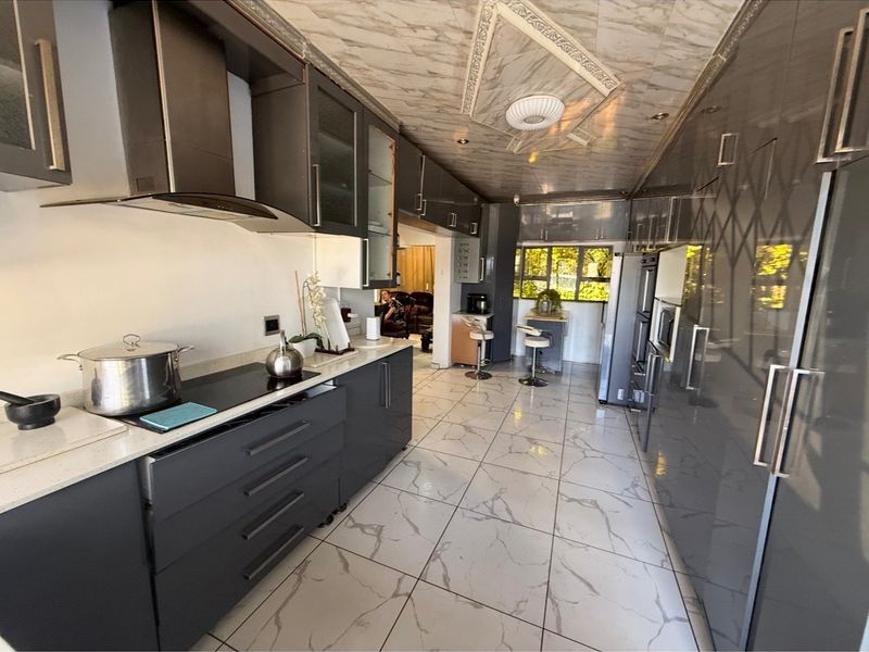 Modern galley-style kitchen featuring dark cabinetry, stone countertops, integrated appliances, and marble-effect floor tiles with a decorative ceiling finish.