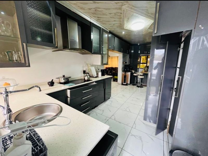 Modern kitchen featuring dark cabinetry, stone countertops, stainless steel sink, integrated cooktop, and polished marble-look floor tiles.
