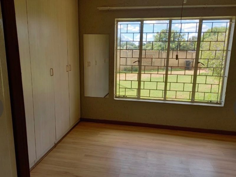 A vacant bedroom featuring laminate flooring, built-in cupboards, and a large window with security bars overlooking the rear garden.