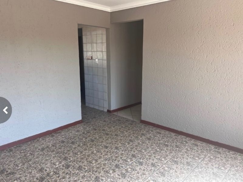 An empty living area featuring neutral textured walls, tiled flooring, and coving, providing a blank canvas for interior design.