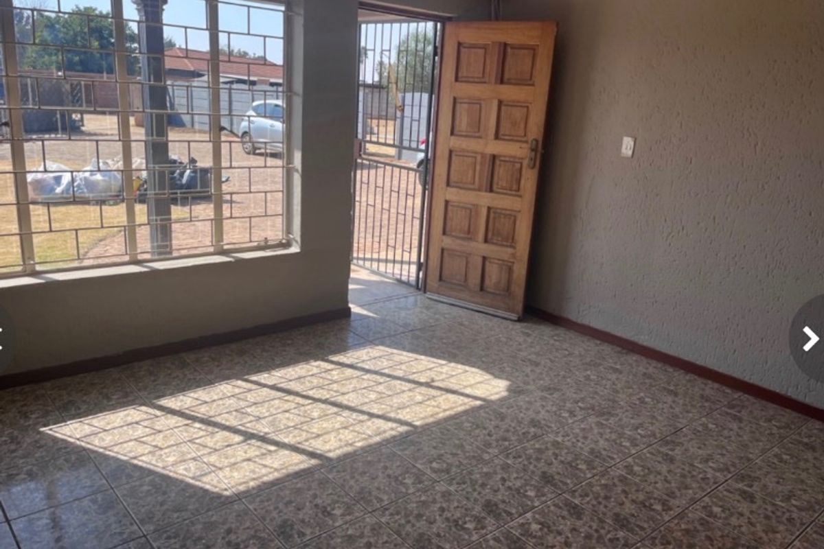 An empty living area featuring tiled flooring, a timber entrance door, and security bars on the windows.