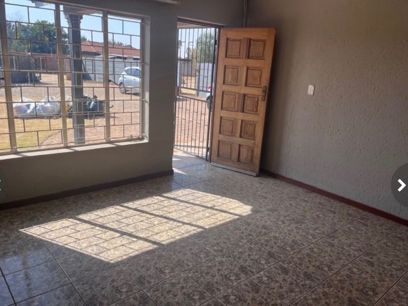 An empty living area featuring tiled flooring, a timber entrance door, and security bars on the windows.