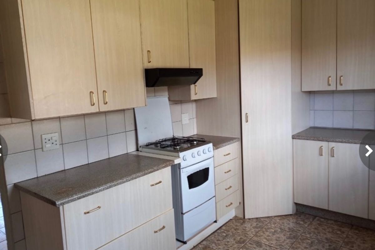 A functional kitchen featuring light wood-look cabinetry, stone-effect countertops, a tiled backsplash, and a freestanding gas stove with an extractor fan.