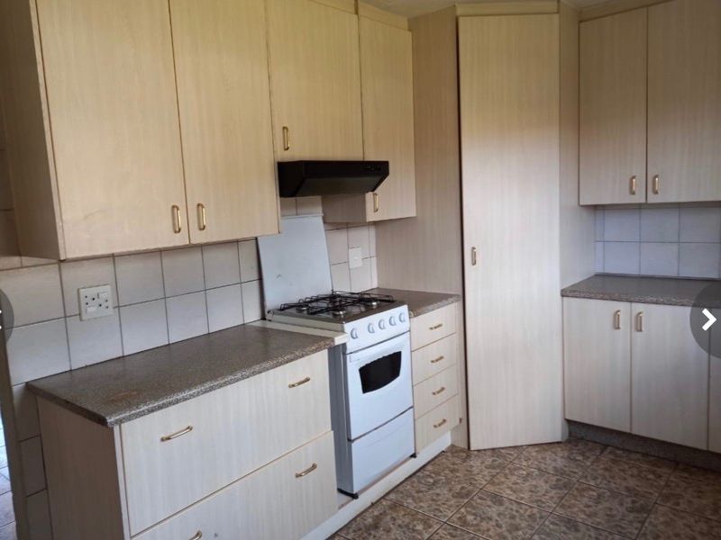 A functional kitchen featuring light wood-look cabinetry, stone-effect countertops, a tiled backsplash, and a freestanding gas stove with an extractor fan.