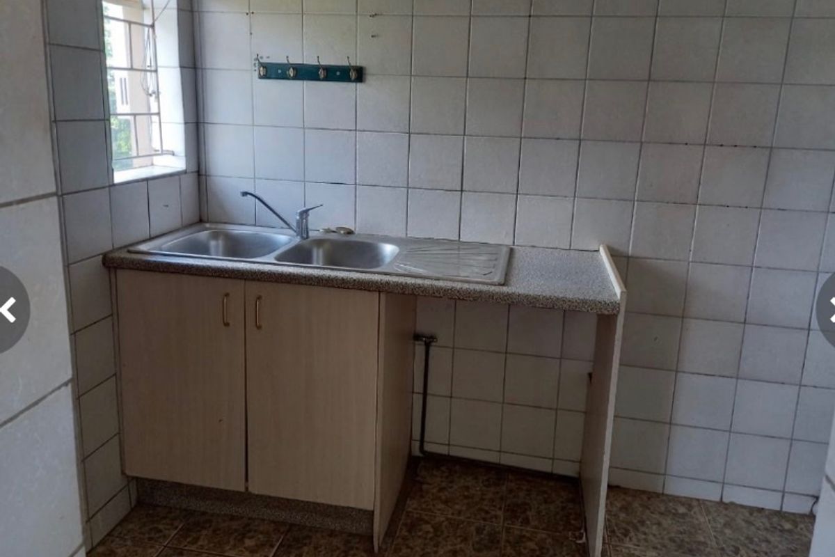 A functional scullery or utility area featuring a double bowl sink, laminate countertop, and full-height wall tiling, offering a practical space for food preparation.