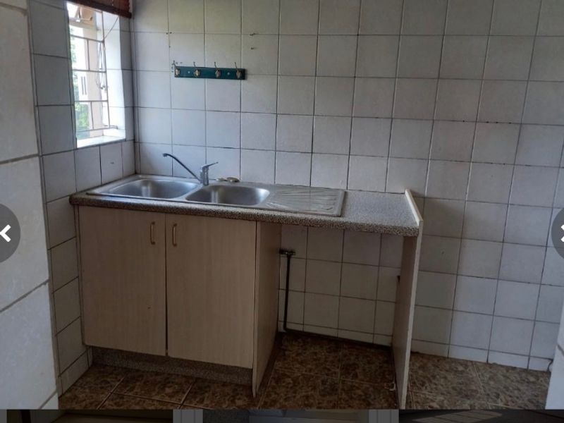A functional scullery or utility area featuring a double bowl sink, laminate countertop, and full-height wall tiling, offering a practical space for food preparation.