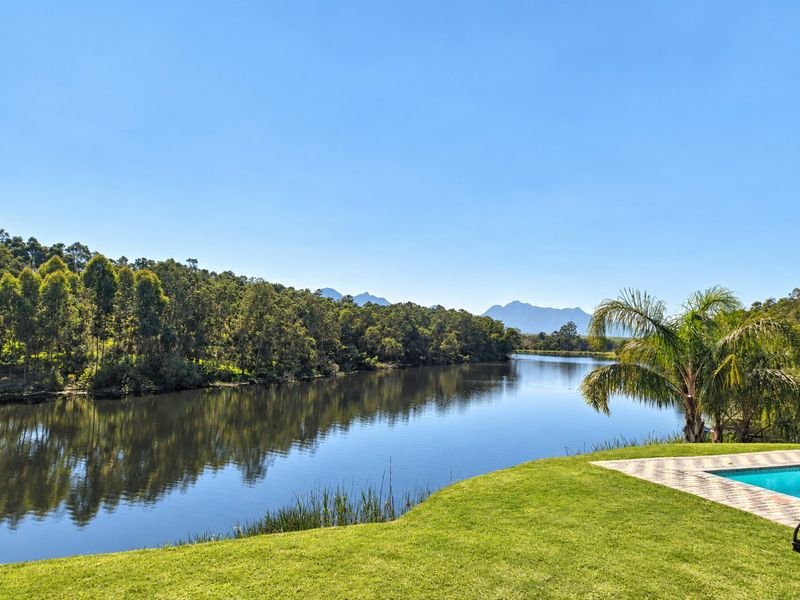 Scenic view overlooking a tranquil lake and distant mountains, featuring a well-maintained lawn and a paved swimming pool area.