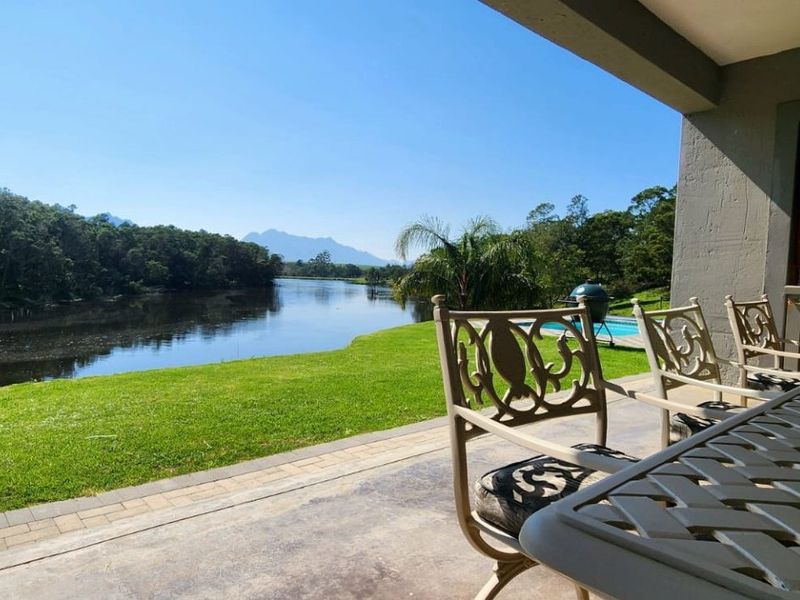 A covered patio area overlooking a scenic river, lush green lawn, and distant mountain views.