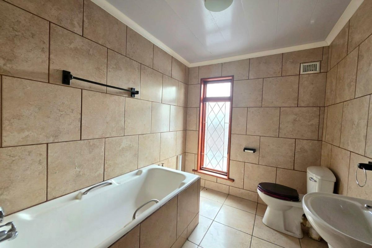 A functional bathroom featuring full-height wall tiling, a bathtub, a pedestal sink, and a leaded glass window providing natural light.