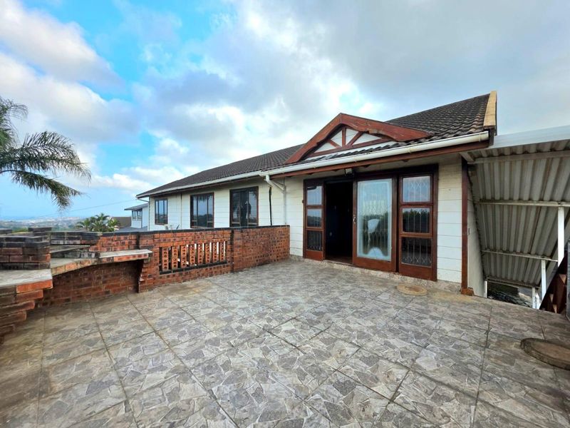 Spacious outdoor patio featuring a built-in brick braai, tiled flooring, and timber-framed glass doors providing access to the main house.