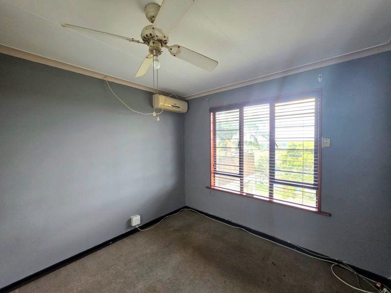 An empty bedroom featuring a ceiling fan, wall-mounted air conditioning unit, and window blinds. The room requires cosmetic updates to the flooring and fixtures.