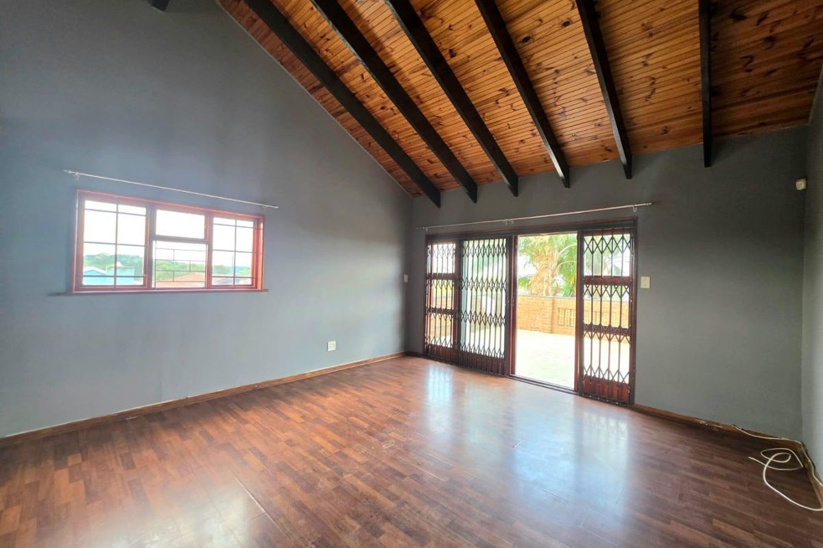 Spacious living area featuring a vaulted timber ceiling with exposed beams, laminate flooring, and sliding doors leading to an outdoor patio.