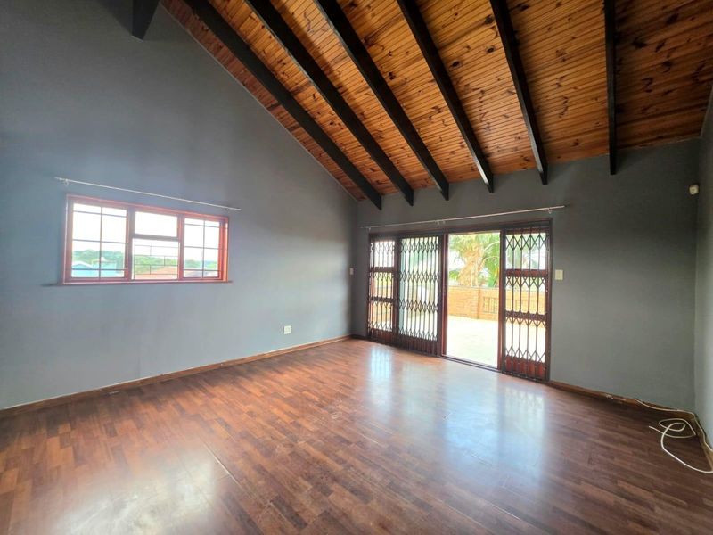 Spacious living area featuring a vaulted timber ceiling with exposed beams, laminate flooring, and sliding doors leading to an outdoor patio.