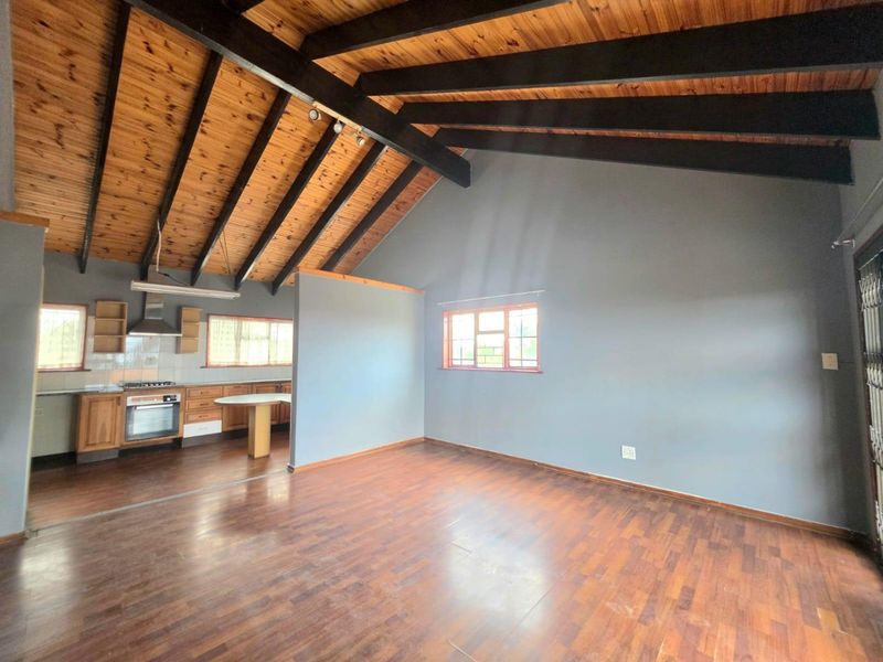 Spacious open-plan living area featuring high vaulted timber ceilings with exposed beams, integrated kitchen cabinetry, and durable laminate flooring throughout.